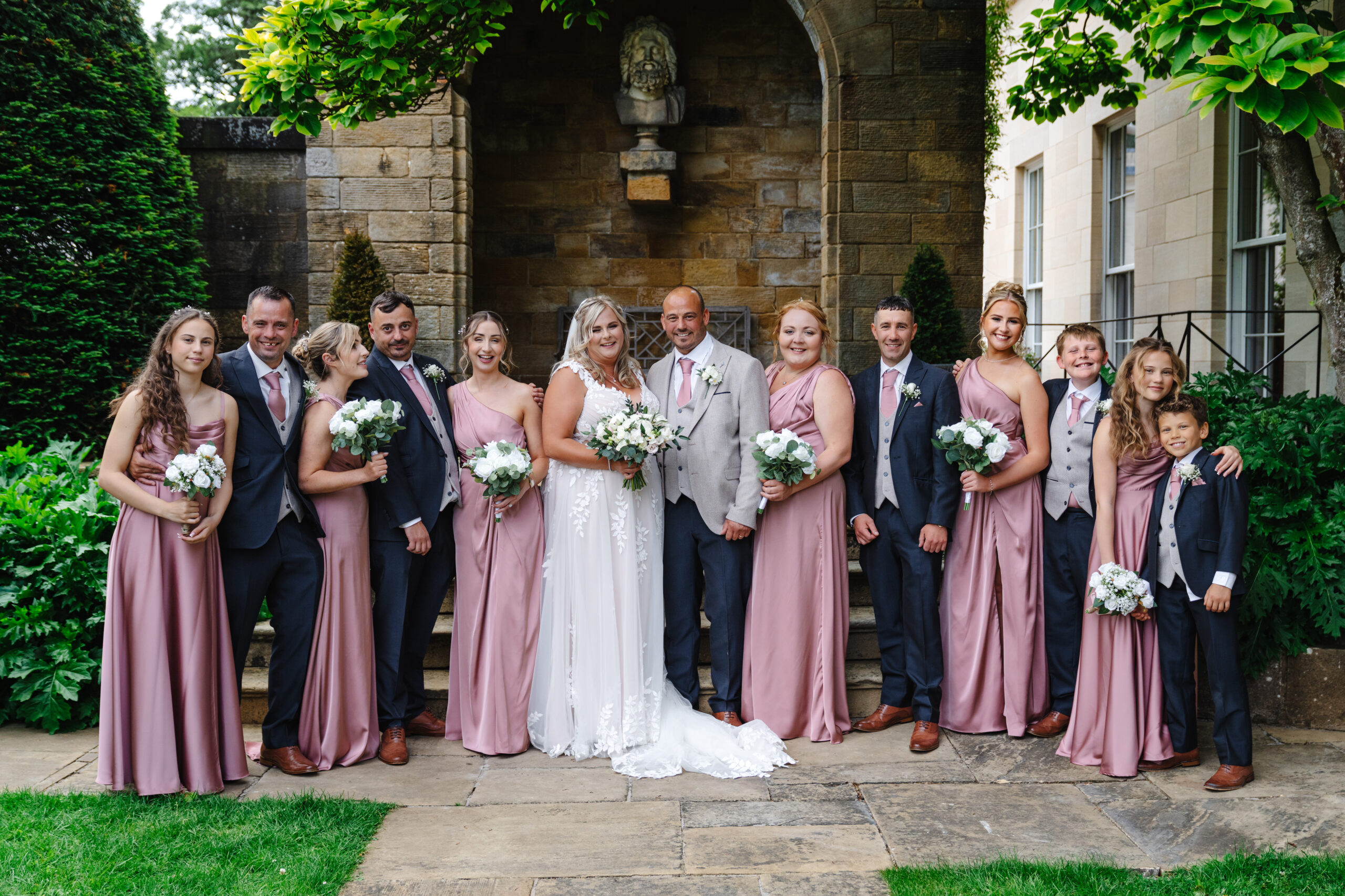 Bride, groom and wedding party beneath a stone arch at Rudding Park in Harrogate