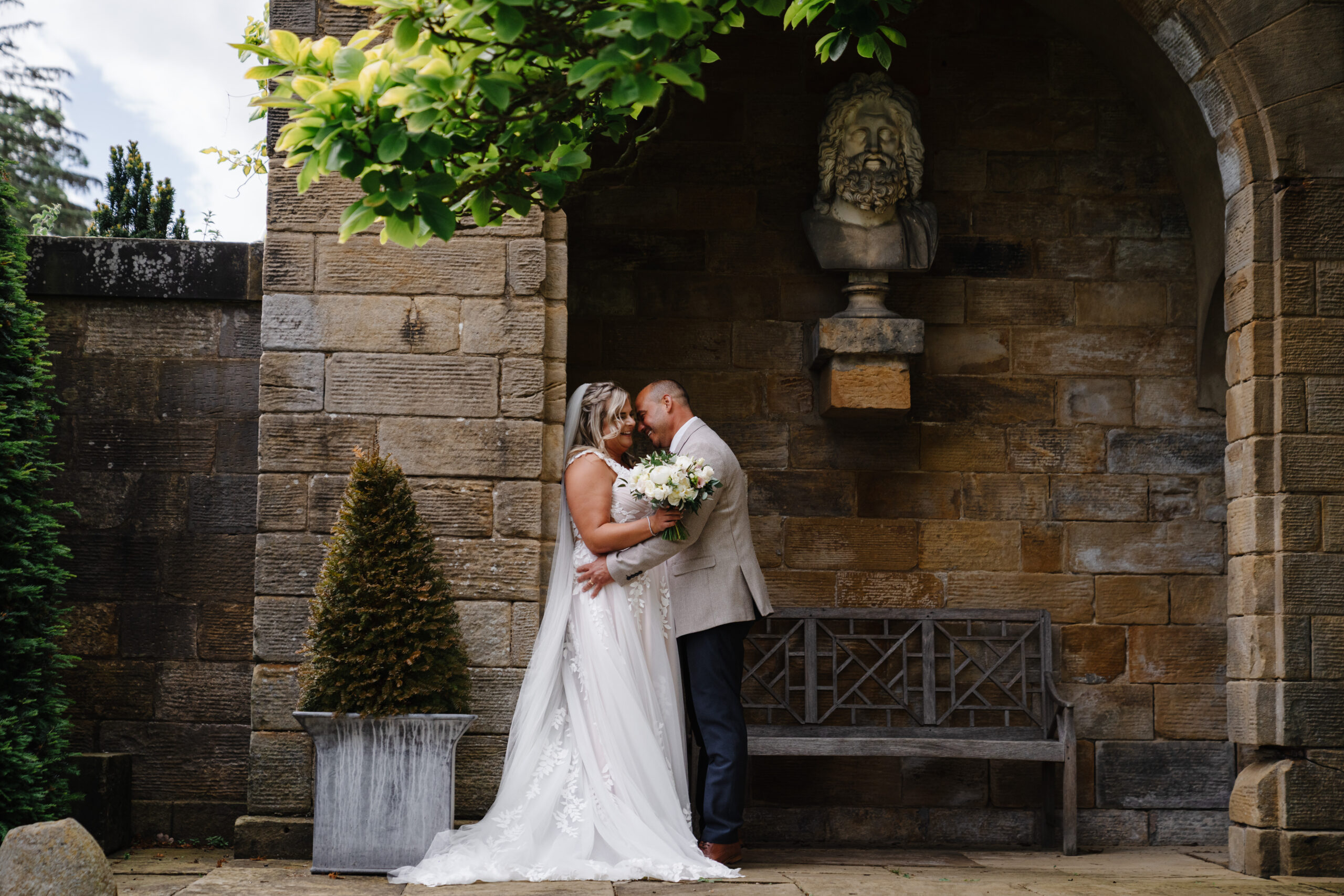 Bride and groom sharing a kiss beneath a stone arch at Rudding Park, Harrogate