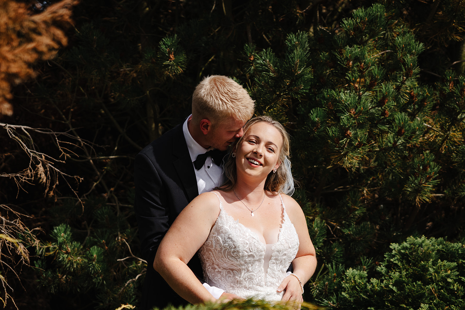 Abbey smiling as Adam kisses her during portraits at Deighton Lodge